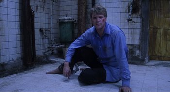 Movie still from “Saw” (2004), directed by James Wan – A man sitting on the ground in a bathroom; Medium shot, Low angle