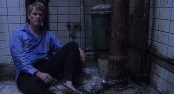 Movie still from “Saw” (2004), directed by James Wan – A man sitting on the ground in a room; Wide shot, High angle