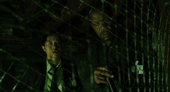 Movie still from “Saw” (2004), directed by James Wan – Two men sitting next to each other in front of barbed wire; Medium shot, Low angle