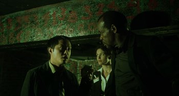 Movie still from “Saw” (2004), directed by James Wan – A group of people standing next to each other in the dark; Medium shot, Low angle