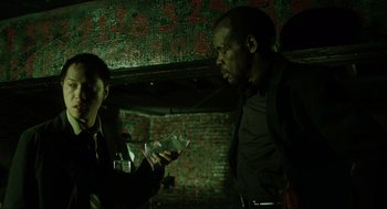 Movie still from “Saw” (2004), directed by James Wan – A man and a woman are looking at something in their hands; Medium shot, Low angle