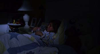 Movie still from “Saw” (2004), directed by James Wan – A little girl laying in a bed holding a remote control; Medium shot, High angle