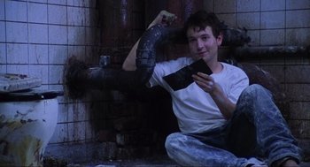 Movie still from “Saw” (2004), directed by James Wan – A man sitting on the ground holding a cell phone; Medium shot, Low angle