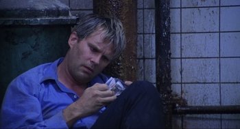 Movie still from “Saw” (2004), directed by James Wan – A man sitting on the ground looking at a cell phone; Close Up shot, High angle