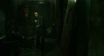 Movie still from “Saw” (2004), directed by James Wan – A man standing in a dark room holding a microphone; Wide shot, High angle