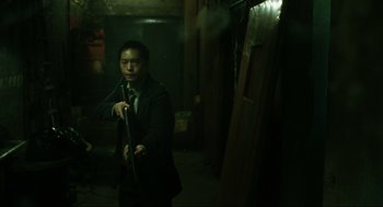 Movie still from “Saw” (2004), directed by James Wan – A man in a suit and tie holding a flute; Medium shot, Low angle