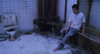 Movie still from “Saw” (2004), directed by James Wan – A man sitting on the ground with his feet chained to a fire hydrant; Wide shot, High angle