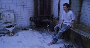 Movie still from “Saw” (2004), directed by James Wan – A man sitting on the ground with his feet chained to a fire hydrant; Wide shot, High angle