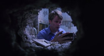 Movie still from “Saw” (2004), directed by James Wan – A man looking at his cell phone through a hole in the wall; Close Up shot, Overhead angle