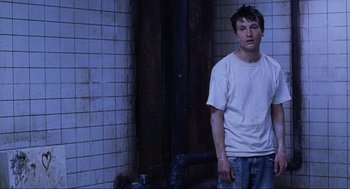Movie still from “Saw” (2004), directed by James Wan – A young man standing in front of a tiled wall; Medium shot, Low angle