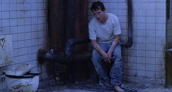 Movie still from “Saw” (2004), directed by James Wan – A man sitting on the ground in front of a fire hydrant; Medium shot, High angle