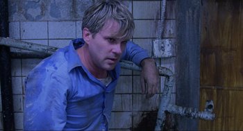 Movie still from “Saw” (2004), directed by James Wan – A man leaning against a pipe in a bathroom; Medium shot, Low angle