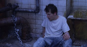 Movie still from “Saw” (2004), directed by James Wan – A man sitting on the ground next to a fire hydrant; Close Up shot, High angle