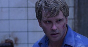 Movie still from “Saw” (2004), directed by James Wan – A person wearing a blue shirt with blood on his face; Close Up shot, Over the shoulder angle