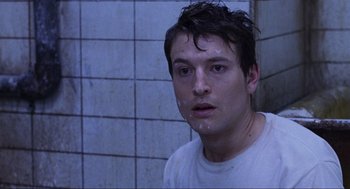 Movie still from “Saw” (2004), directed by James Wan – A young man with wet hair and a white t - shirt in a bathroom; Close Up shot, High angle