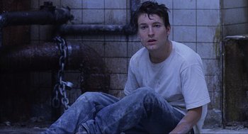 Movie still from “Saw” (2004), directed by James Wan – A man sitting on the ground in front of a fire hydrant; Close Up shot, High angle