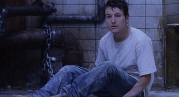 Movie still from “Saw” (2004), directed by James Wan – A man sitting on the ground in front of a fire hydrant; Medium shot, High angle