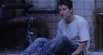 Movie still from “Saw” (2004), directed by James Wan – A man sitting on the ground next to a fire hydrant; Medium shot, High angle