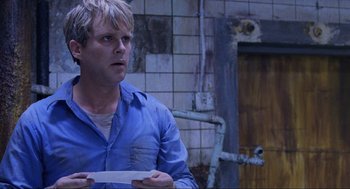 Movie still from “Saw” (2004), directed by James Wan – A man in a blue shirt is holding a piece of paper in his hand; Close Up shot, Over the shoulder angle