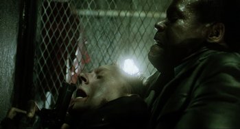 Movie still from “Saw” (2004), directed by James Wan – A man holding a knife next to another man in a cage; Close Up shot, Low angle