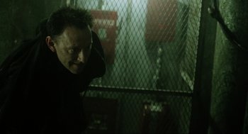 Movie still from “Saw” (2004), directed by James Wan – A man standing next to a chain link fence in the dark; Close Up shot, Low angle