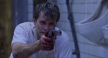 Movie still from “Saw” (2004), directed by James Wan – A man holding a gun with blood on his face; Close Up shot, High angle