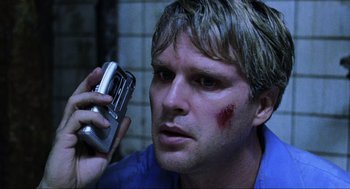 Movie still from “Saw” (2004), directed by James Wan – A man with blood on his face holding up a cell phone; Close Up shot, High angle