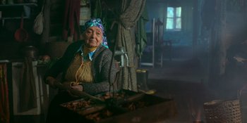 Movie still from “Sayen” (2023), directed by Alexander Witt – An older woman sitting in a chair in a room; Medium shot, Low angle