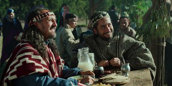 Movie still from “Sayen” (2023), directed by Alexander Witt – A group of men sitting at a table eating food; Medium shot, Over the shoulder angle