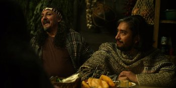 Movie still from “Sayen” (2023), directed by Alexander Witt – Two men sitting at a table with food on the table; Medium shot, Over the shoulder angle