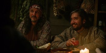 Movie still from “Sayen” (2023), directed by Alexander Witt – A couple of men sitting at a dinner table together; Medium shot, Over the shoulder angle