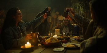 Movie still from “Sayen” (2023), directed by Alexander Witt – A group of people sitting at a table with food and drinks; Medium shot, Low angle