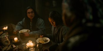 Movie still from “Sayen” (2023), directed by Alexander Witt – A group of people sitting at a table with plates of food; Medium shot, Over the shoulder angle