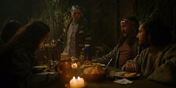 Movie still from “Sayen” (2023), directed by Alexander Witt – A group of people sitting at a table with food on it; Medium shot, Over the shoulder angle