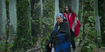 Movie still from “Sayen” (2023), directed by Alexander Witt – Two women walking in the woods wearing blankets; Wide shot, Over the shoulder angle