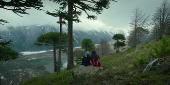 Movie still from “Sayen” (2023), directed by Alexander Witt – Two people sitting on a rock near a tree; Extreme Wide shot, High angle