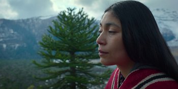 Movie still from “Sayen” (2023), directed by Alexander Witt – A woman in a red and white jacket looking at a tree; Close Up shot, Low angle
