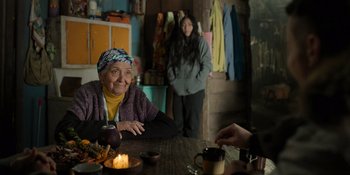 Movie still from “Sayen” (2023), directed by Alexander Witt – An older woman sitting at a table with a cup of tea; Medium shot, Over the shoulder angle