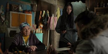 Movie still from “Sayen” (2023), directed by Alexander Witt – A group of people sitting at a table in a room; Medium shot, Over the shoulder angle
