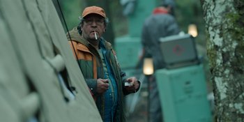 Movie still from “Sayen” (2023), directed by Alexander Witt – An older man smoking a cigarette while standing next to a teepee; Medium shot, Low angle
