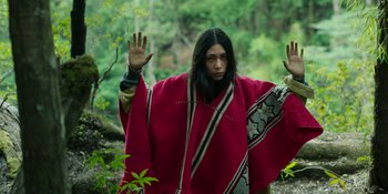 Movie still from “Sayen” (2023), directed by Alexander Witt – A man in a red poncho is holding his hands up in the air; Medium shot, Low angle