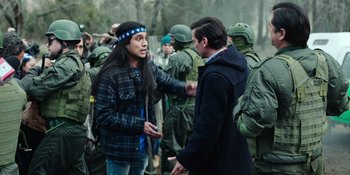 Movie still from “Sayen” (2023), directed by Alexander Witt – A man in a headband and a man in a jacket are talking to each other in front of a group of soldiers; Medium shot, Over the shoulder angle