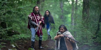 Movie still from “Sayen” (2023), directed by Alexander Witt – A group of people in the woods with a blanket; Medium shot, Over the shoulder angle