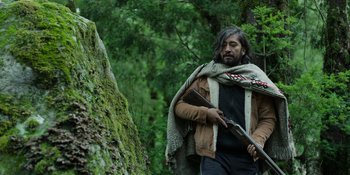 Movie still from “Sayen” (2023), directed by Alexander Witt – A man holding a rifle in a wooded area; Medium shot, Low angle