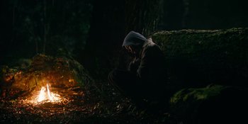 Movie still from “Sayen” (2023), directed by Alexander Witt – A person sitting on a rock in the dark; Wide shot, High angle