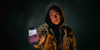 Movie still from “Sayen” (2023), directed by Alexander Witt – A person holding a cell phone in their hand; Medium shot, Low angle