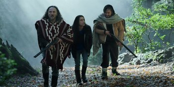 Movie still from “Sayen” (2023), directed by Alexander Witt – A group of people walking through a forest; Medium shot, Low angle