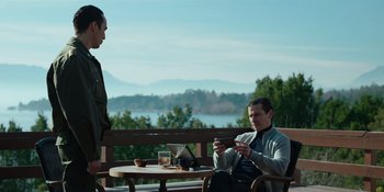 Movie still from “Sayen” (2023), directed by Alexander Witt – Two men are sitting at a table and one of them is holding a cell phone; Medium shot, Low angle