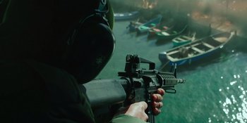 Movie still from “Sayen” (2023), directed by Alexander Witt – A person with a gun in front of a body of water; Medium shot, High angle