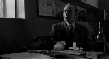 Movie still from “Schindler's List” (1993), directed by Steven Spielberg – An older man sitting at a table with a phone; Medium shot, Low angle